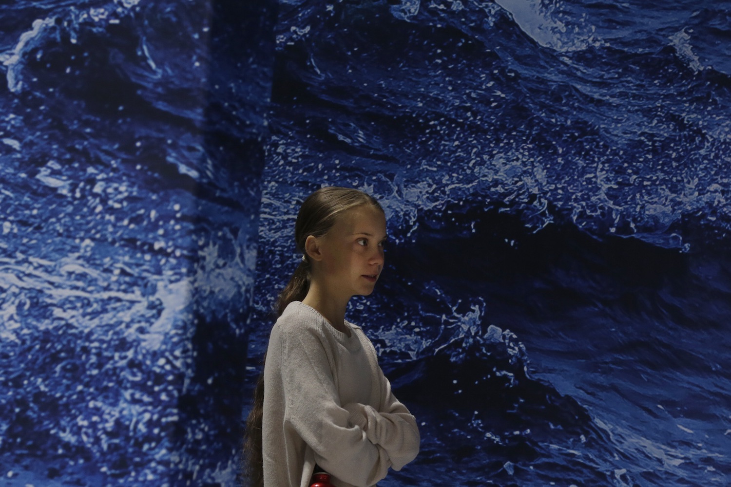 Greta Thunberg standing in front of a large poster of the ocean
