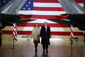 President Trump and First Lady Melania Trump walk by fighter jets in front of a big American flag
