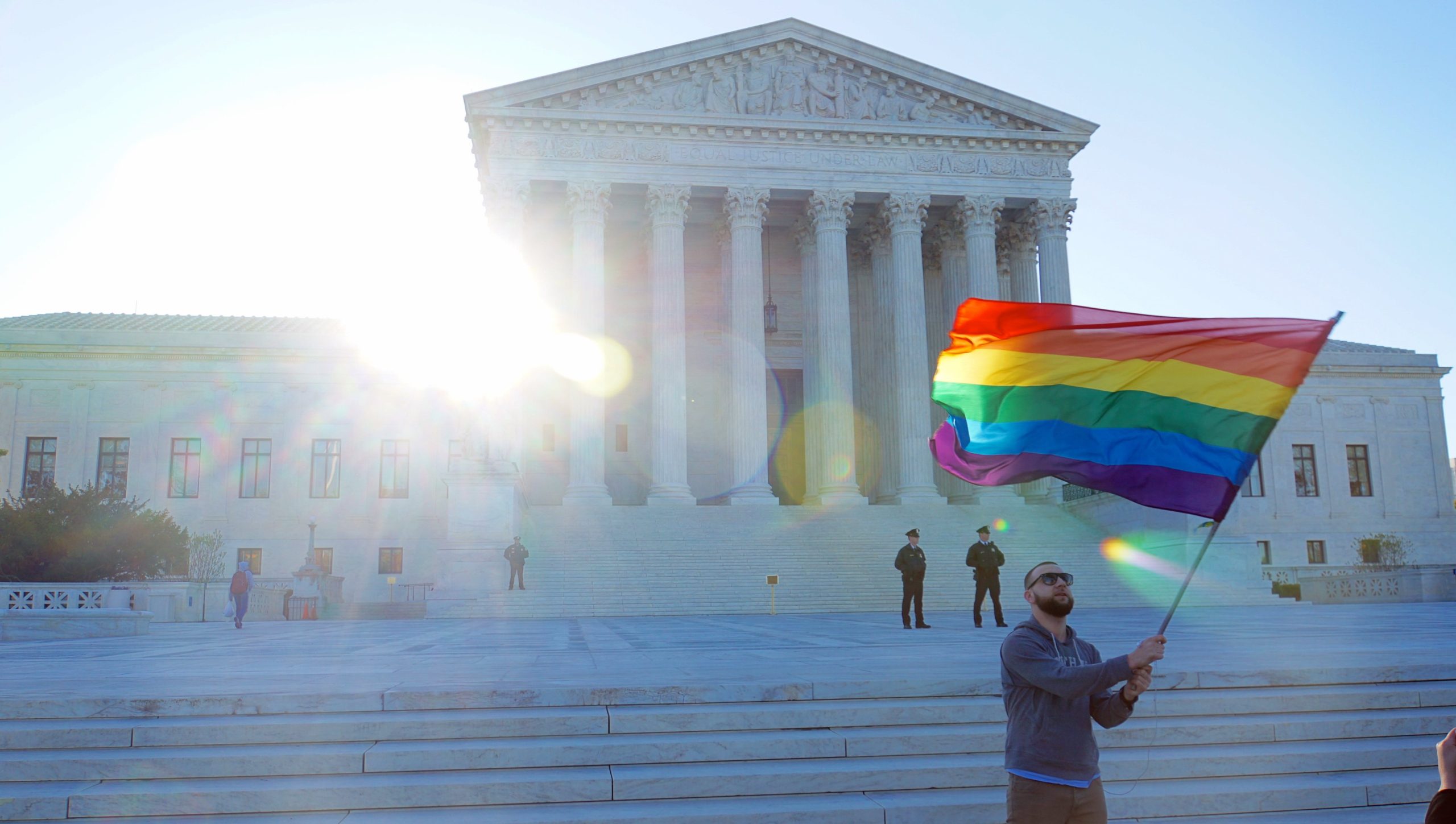 LGBTQ+ flag being waved in front of the U.S. Supreme Court.