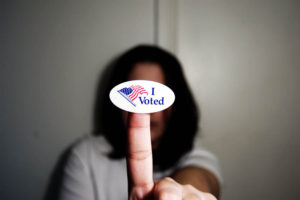 A woman holds up an "I voted" sticker with the U.S. flag on it.