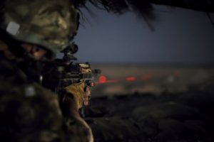 A soldier points a weapon with a laser.