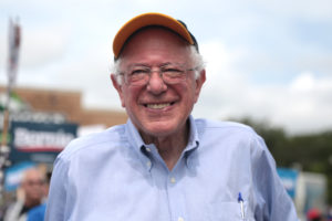 Bernie Sanders smiles, wearing a baseball cap.