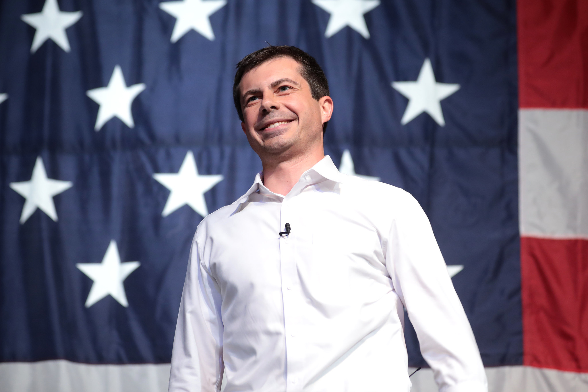 Democratic candidate Pete Buttigieg smiling in front of a U.S. flag.