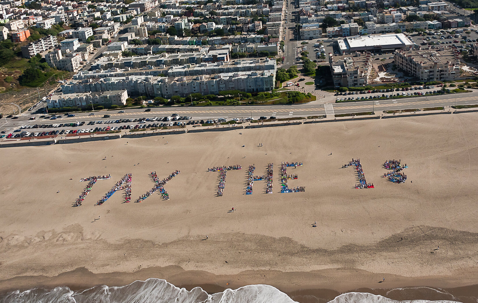 People on a beach spell out the phrase "Tax the 1%."