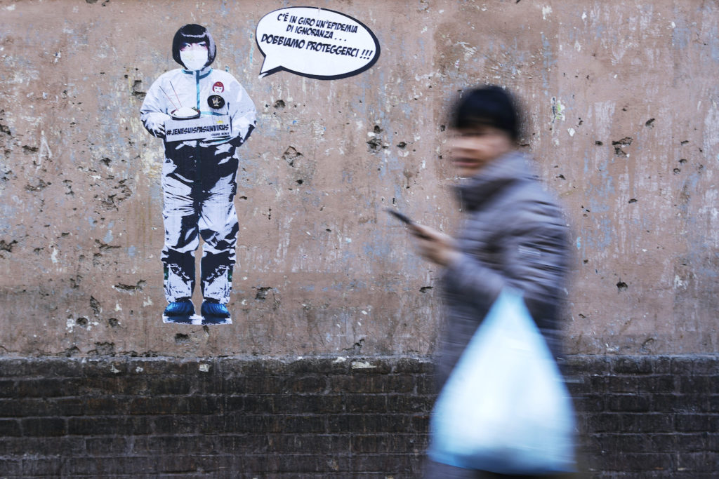 A person walking by a wall featuring street art commenting on ignorance vis-a-vis the coronavirus outbreak