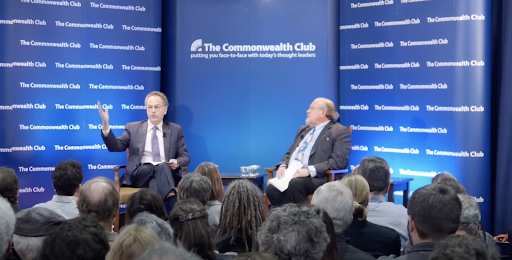 Richard Rockefeller (left) speaking to Larry Brilliant (right) before a large audience