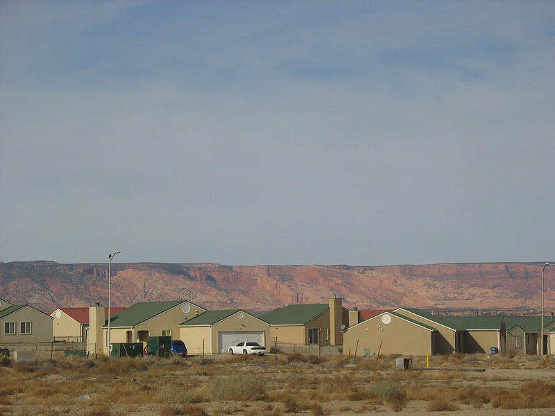 Several uniform brown houses and cars in driveways. A sunlit mountain in the background. Blue sky above everything.
