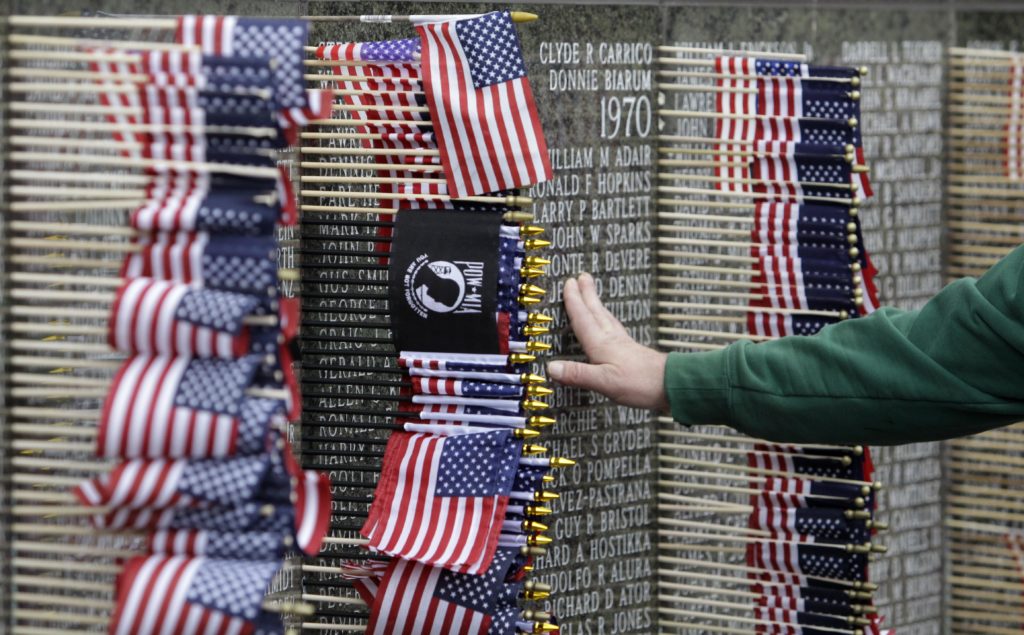 A hand rests against a memorial which is decorated by American flags and a POW/MIA flag.