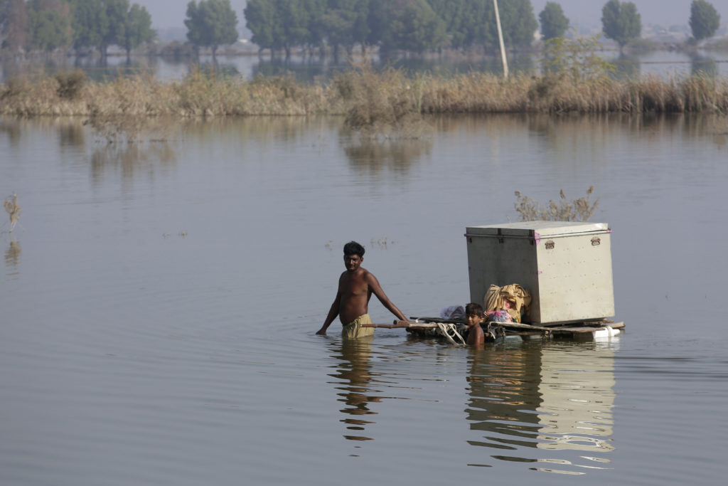A Pakistani man and a young boy wade through waist-deep water in Pakistan after the recent floods, dragging a wooden raft behind them piled high with their belongings.
