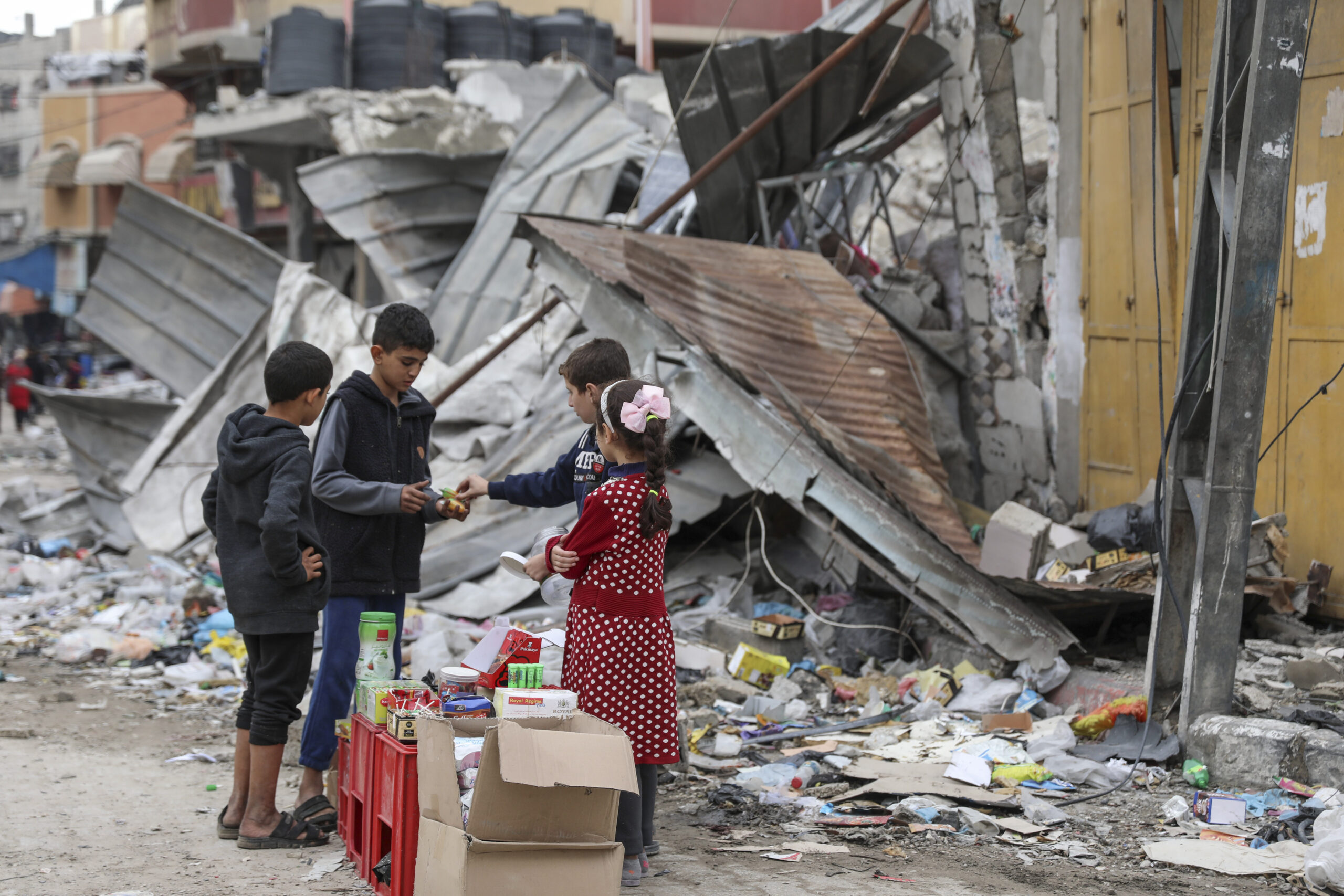 Two Palestinian children with their backs to the camera sell candy at a makeshift candy stand to two other Palestinian children in front of a demolished building in the Jebaliya refugee camp in Gaza.